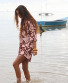 Woman with brown hair wearing a button up dress in blush and brown hibiscus print