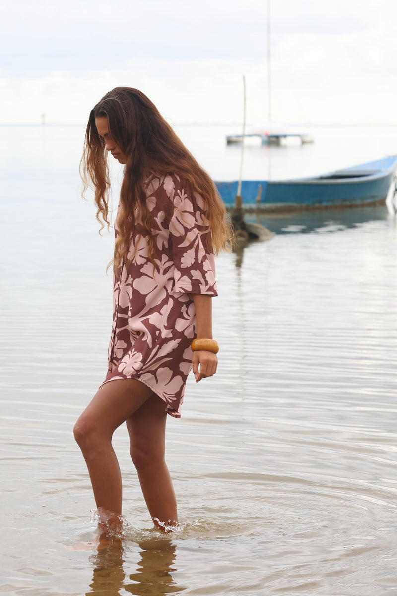 Woman with brown hair wearing a button up dress in blush and brown hibiscus print
