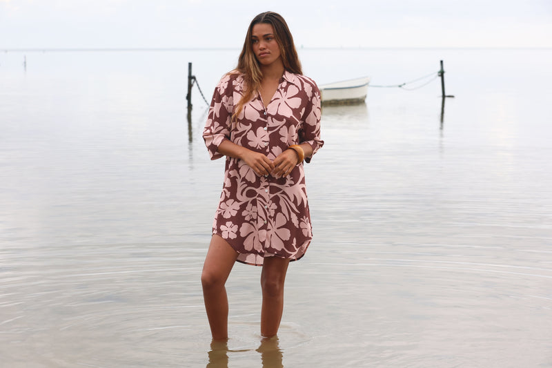 Woman with brown hair wearing a button up dress in blush and brown hibiscus print