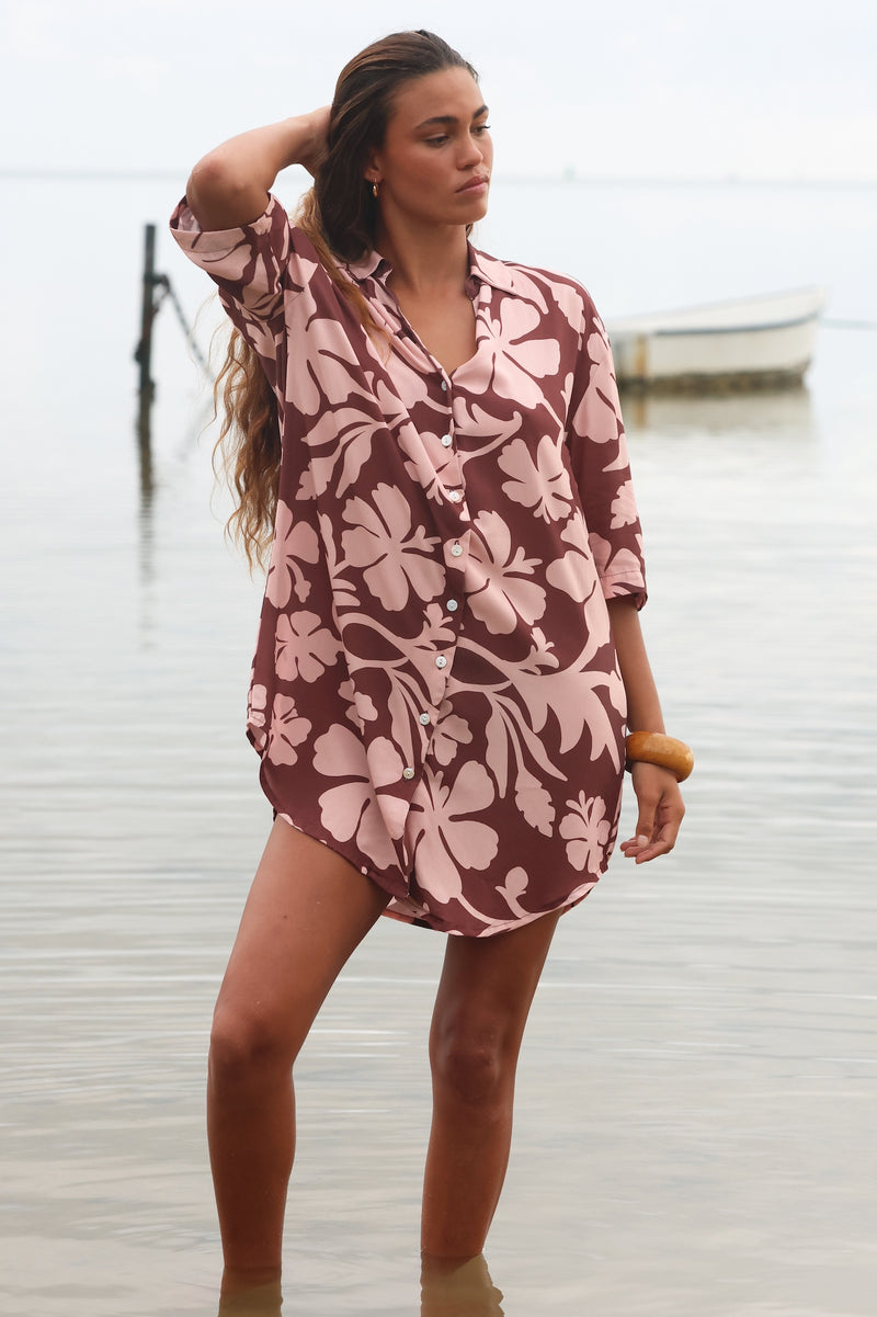 Woman with brown hair wearing a button up dress in blush and brown hibiscus print