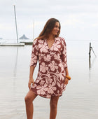 Woman with brown hair wearing a button up dress in blush and brown hibiscus print