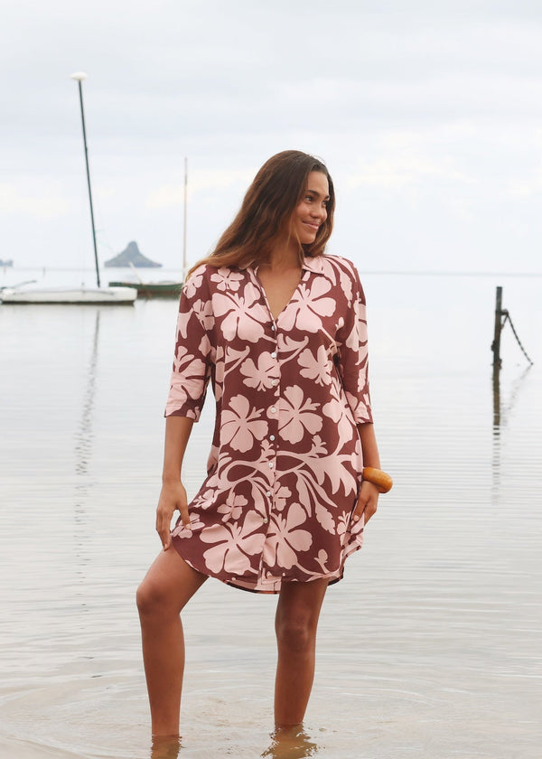 Woman with brown hair wearing a button up dress in blush and brown hibiscus print