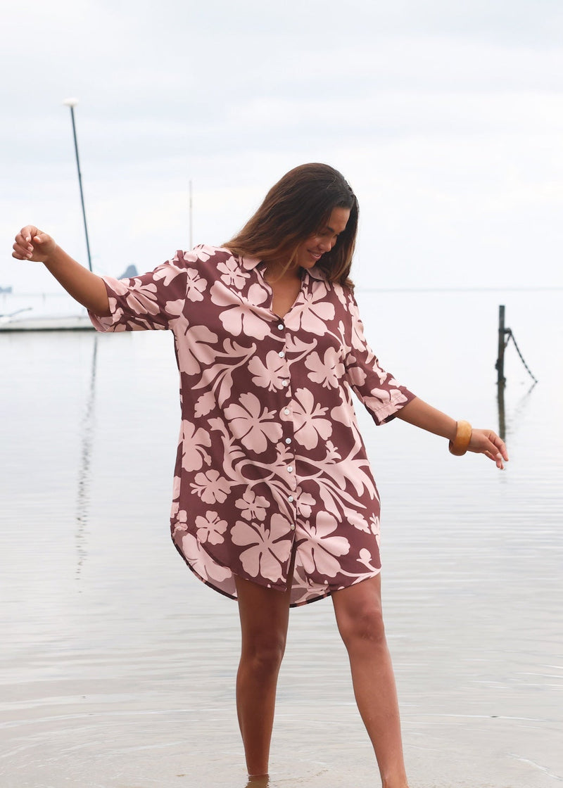 Woman with brown hair wearing a button up dress in blush and brown hibiscus print