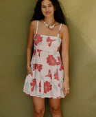 Woman wearing sleeveless short tiered dress with large red and light blue floral print on beige ground.