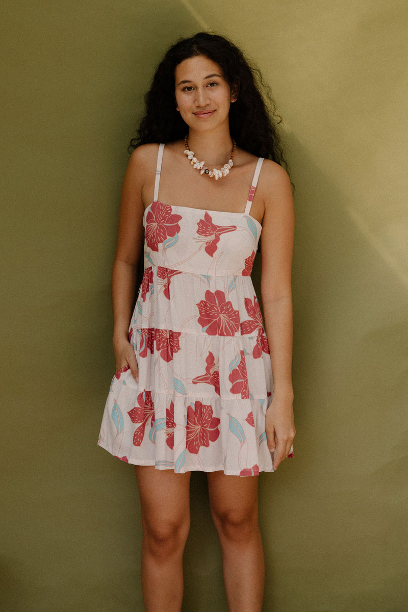 Woman wearing sleeveless short tiered dress with large red and light blue floral print on beige ground.