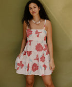 Woman wearing sleeveless short tiered dress with large red and light blue floral print on beige ground.