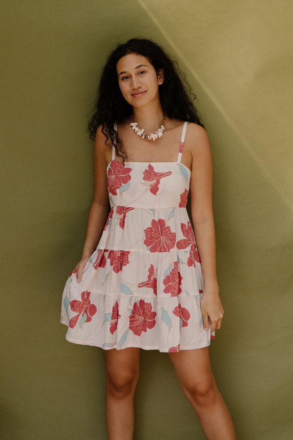 Woman wearing sleeveless short tiered dress with large red and light blue floral print on beige ground.