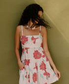 Woman wearing sleeveless short tiered dress with large red and light blue floral print on beige ground.