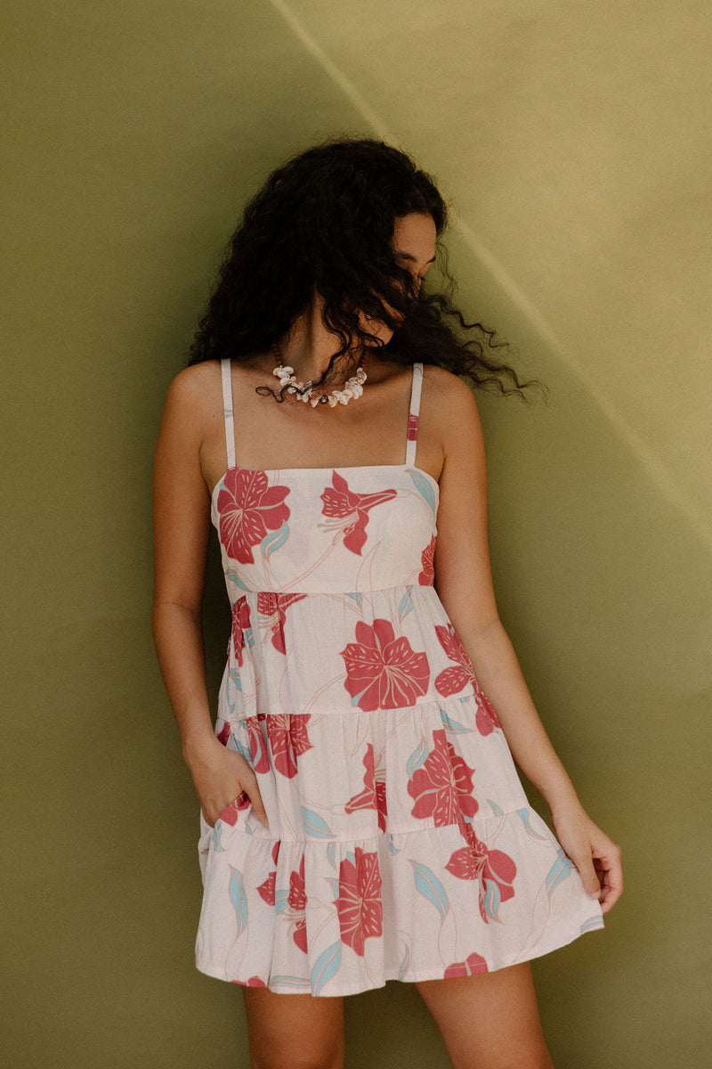 Woman wearing sleeveless short tiered dress with large red and light blue floral print on beige ground.