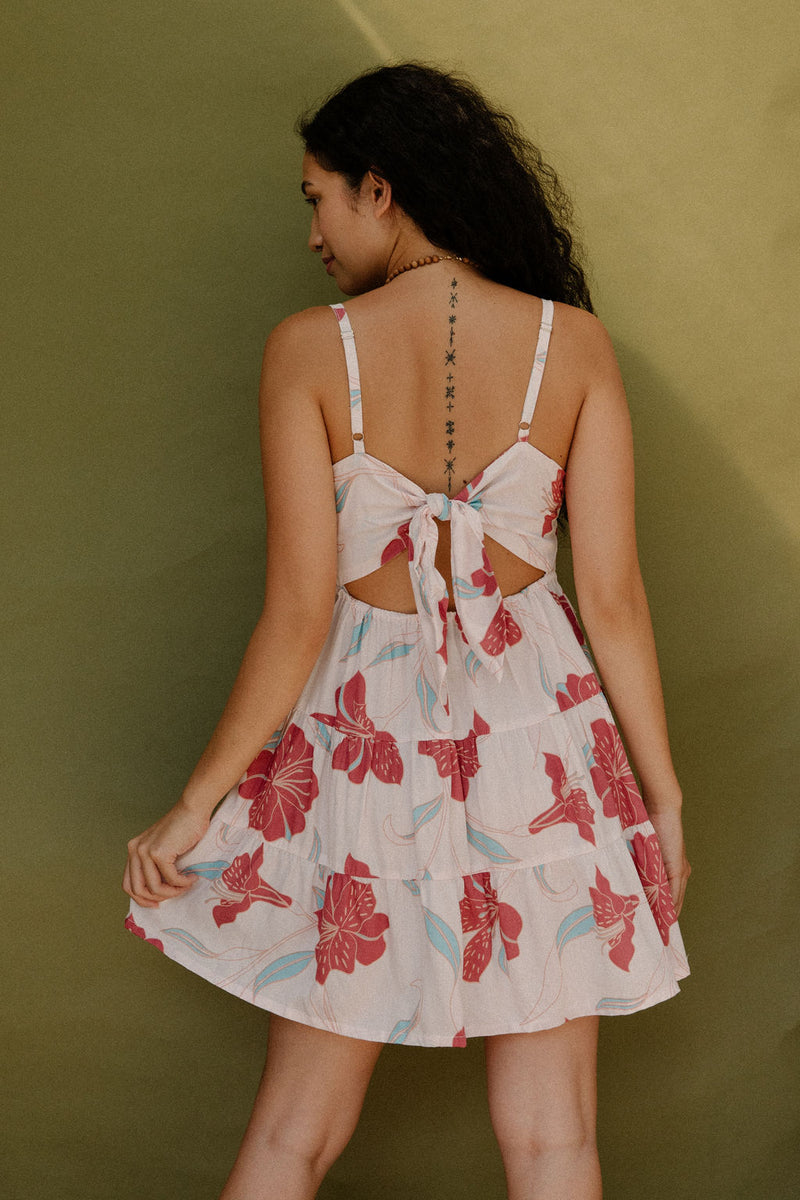 Woman wearing sleeveless short tiered dress with large red and light blue floral print on beige ground.