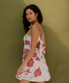 Woman wearing sleeveless short tiered dress with large red and light blue floral print on beige ground.