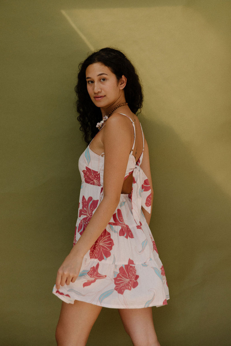 Woman wearing sleeveless short tiered dress with large red and light blue floral print on beige ground.