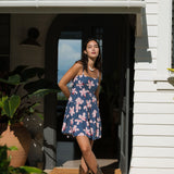 woman with black hair wearing a mini tiered dress with tie back in a navy color with pink hibiscus blossoms 