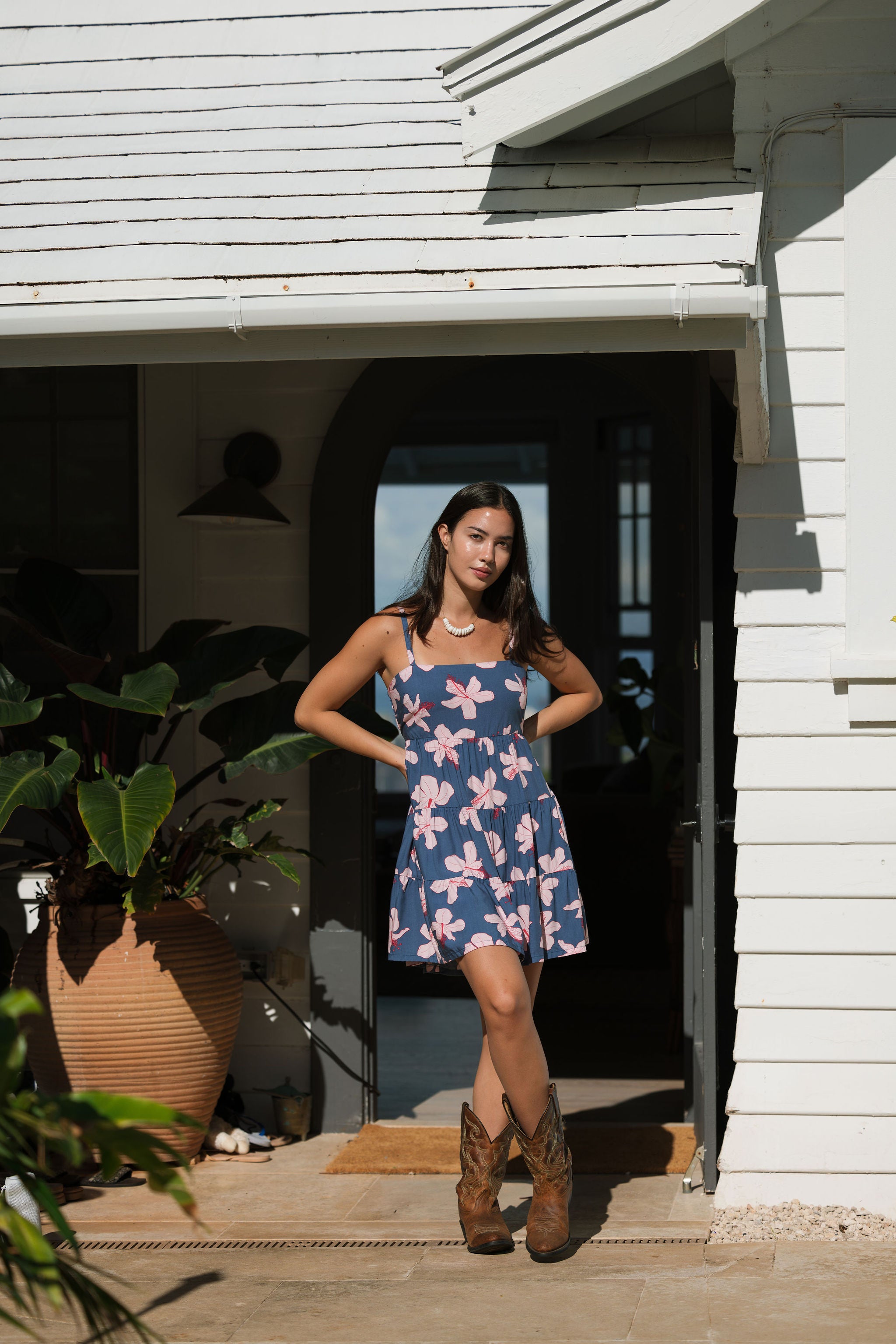 woman with black hair wearing a mini tiered dress with tie back in a navy color with pink hibiscus blossoms 