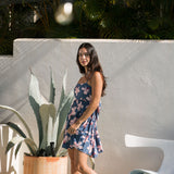 woman with black hair wearing a mini tiered dress with tie back in a navy color with pink hibiscus blossoms 