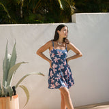 woman with black hair wearing a mini tiered dress with tie back in a navy color with pink hibiscus blossoms 