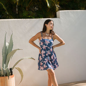 woman with black hair wearing a mini tiered dress with tie back in a navy color with pink hibiscus blossoms 