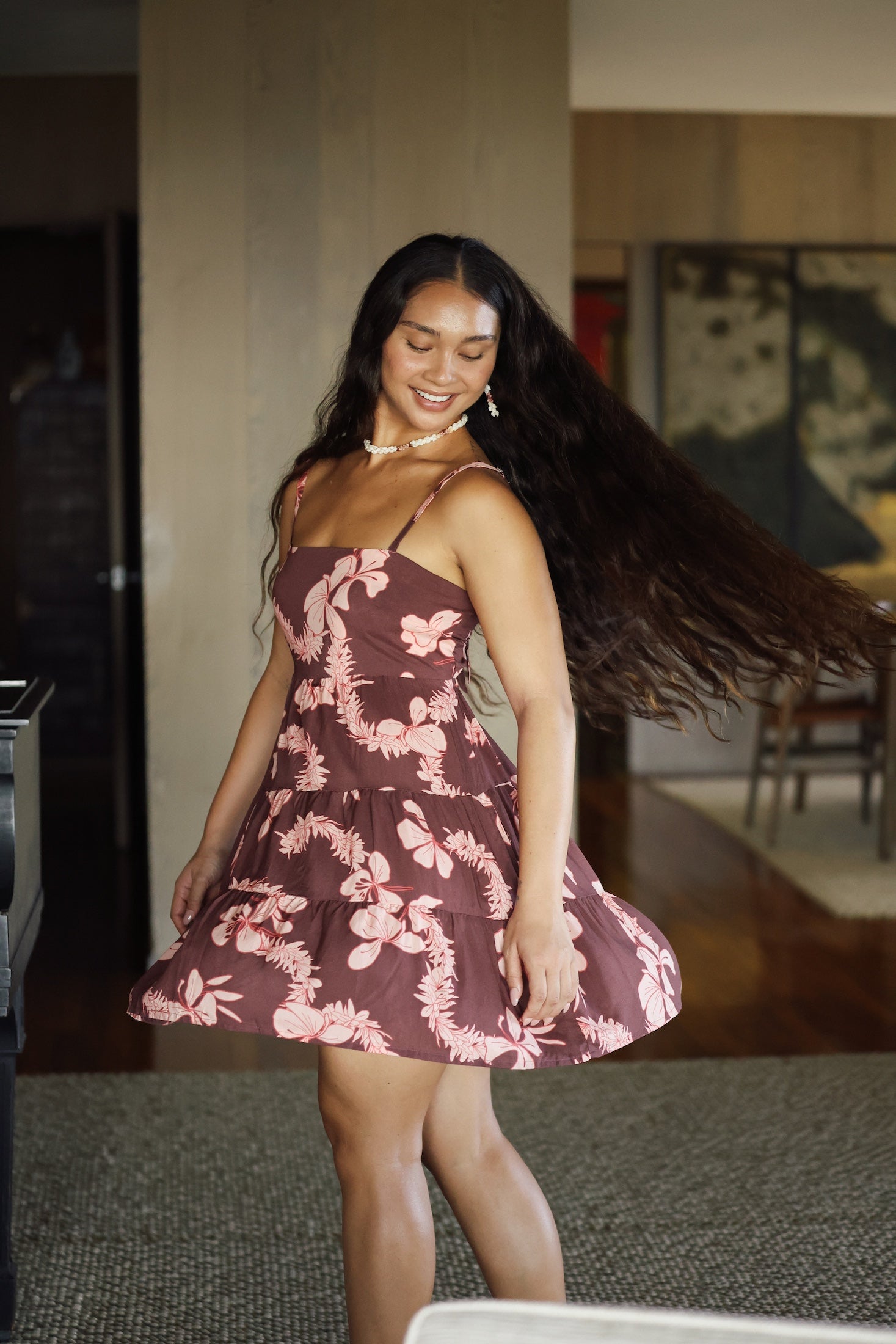 woman with brown hair wearing a brown colored tie back mini dress  with light pink lei awapuhi print