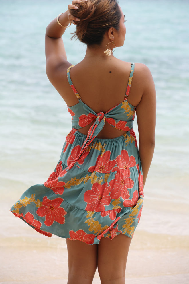 woman with brown hair wearing tie back neck dress with orange and yellow lei pua print