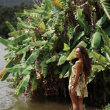 woman with brown hair wearing a mini dress with a tie back in a green color with naupaka pattern throughout. 