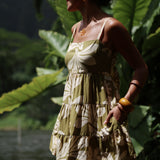 woman with brown hair wearing a mini dress with a tie back in a green color with naupaka pattern throughout. 