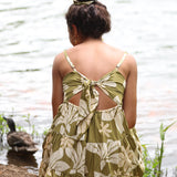woman with brown hair wearing a mini dress with a tie back in a green color with naupaka pattern throughout. 
