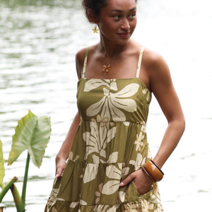 woman with brown hair wearing a mini dress with a tie back in a green color with naupaka pattern throughout. 