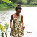 woman with brown hair wearing a mini dress with a tie back in a green color with naupaka pattern throughout. 