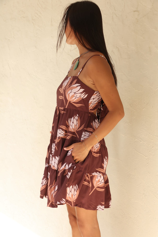 woman wearing a brown colored mini dress with tie back detail and protea print