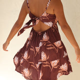 woman wearing a brown colored mini dress with tie back detail and protea print