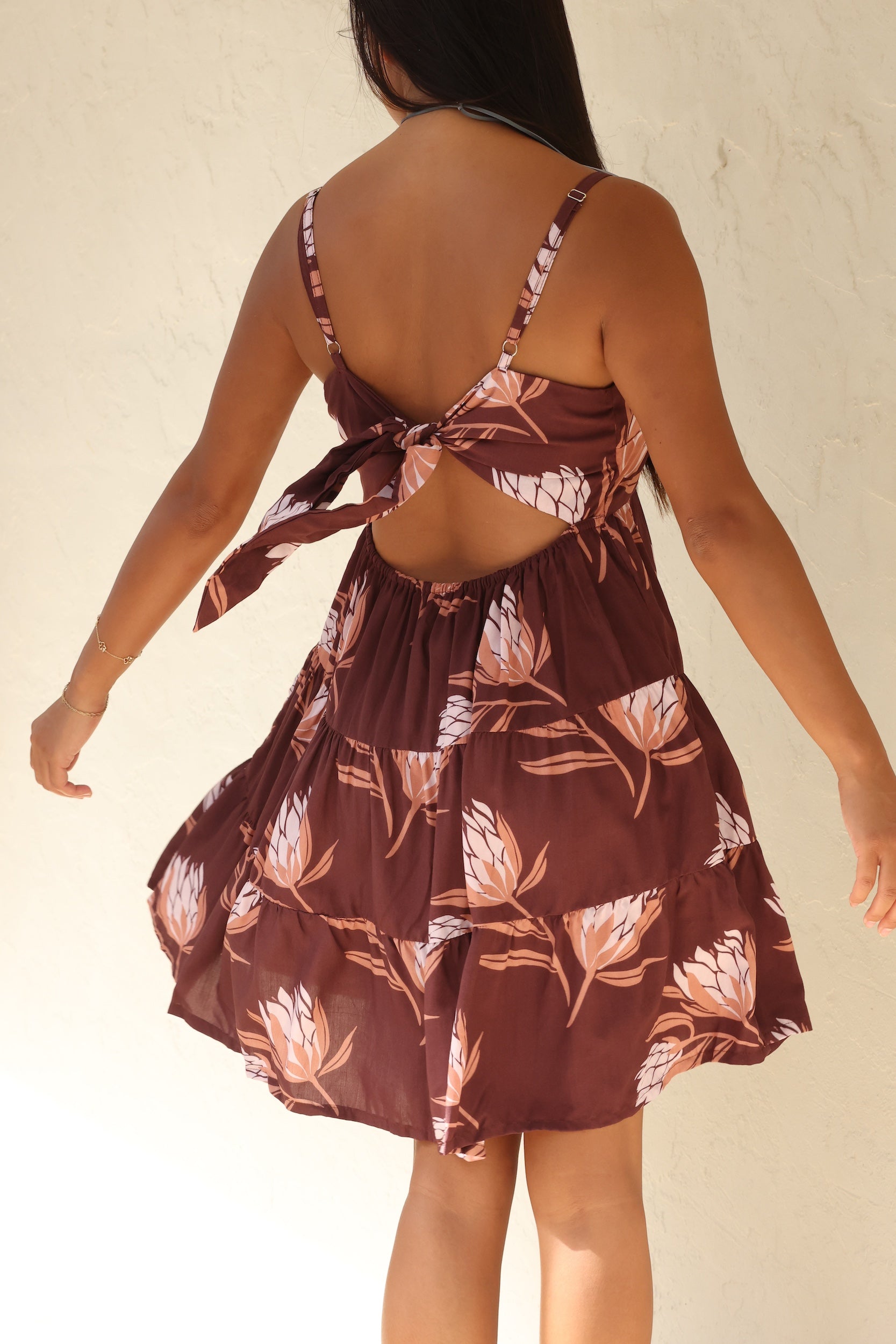 woman wearing a brown colored mini dress with tie back detail and protea print