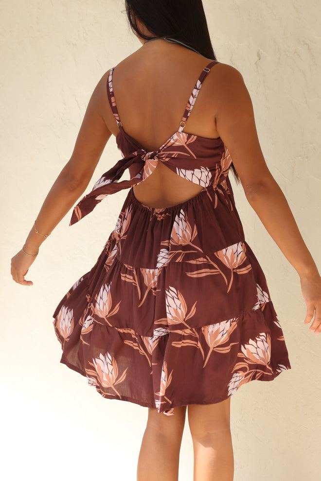 woman wearing a brown colored mini dress with tie back detail and protea print