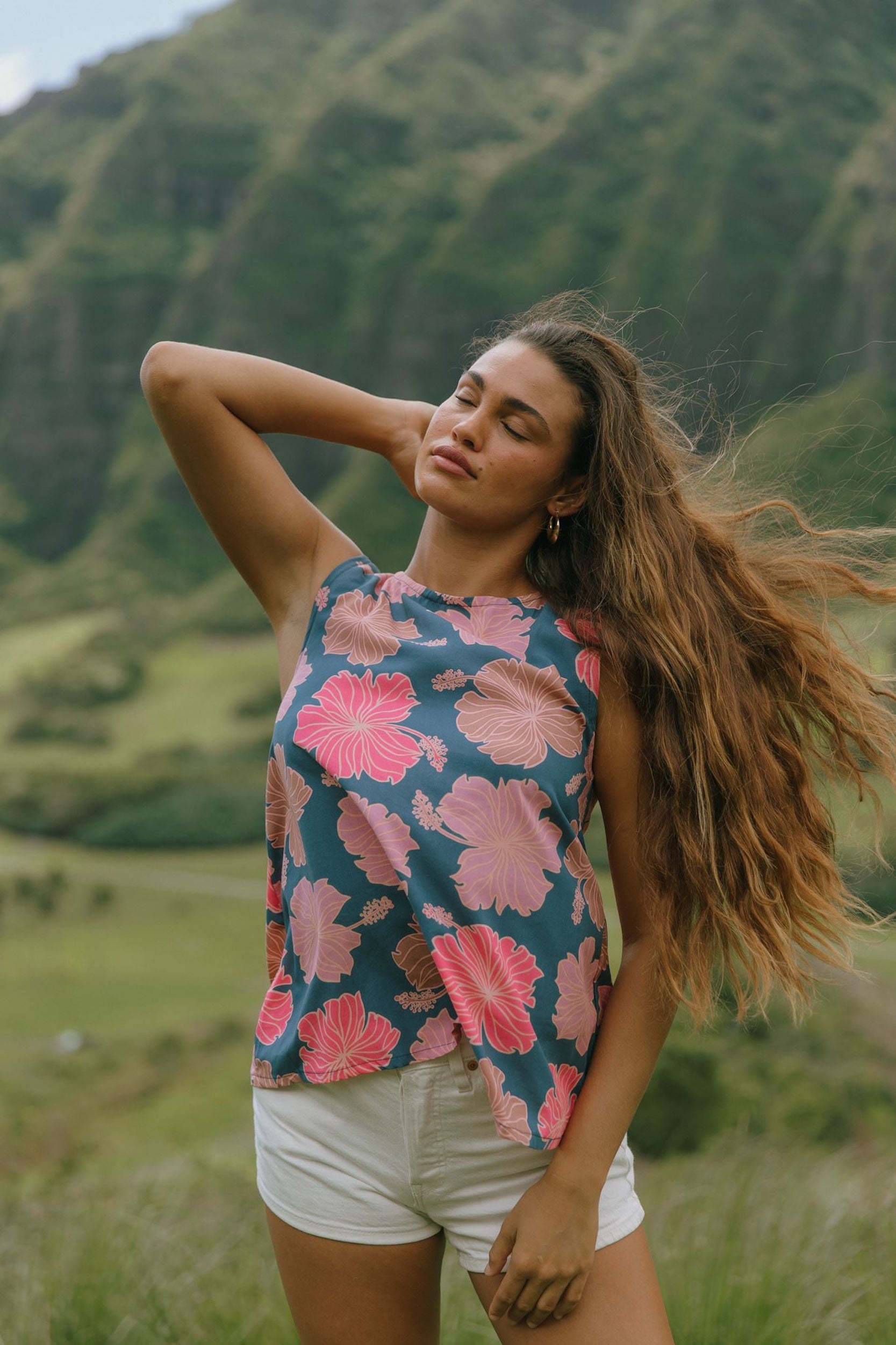 woman with brown hair wearing a navy high neck sleeveless top with bright pink hibiscus print