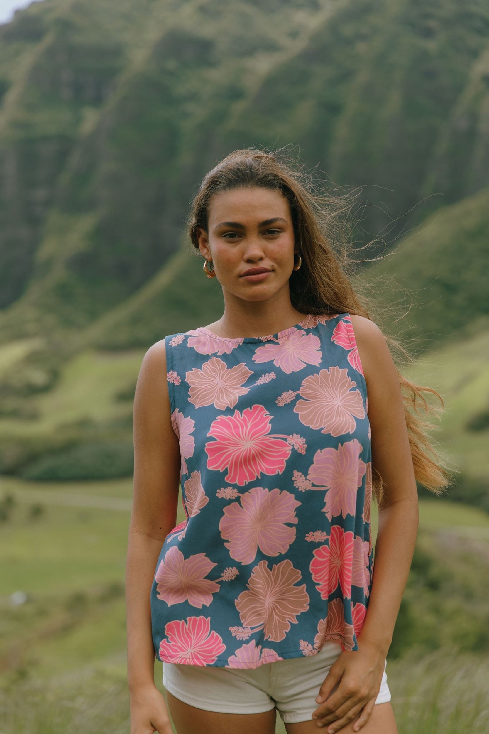 woman with brown hair wearing a navy high neck sleeveless top with bright pink hibiscus print