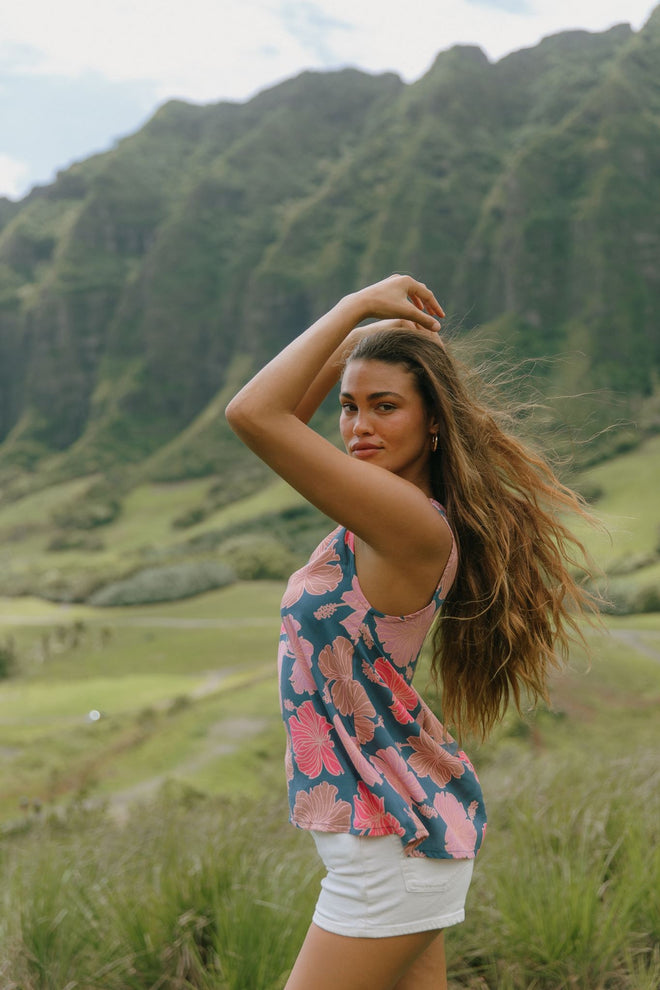 woman with brown hair wearing a navy high neck sleeveless top with bright pink hibiscus print