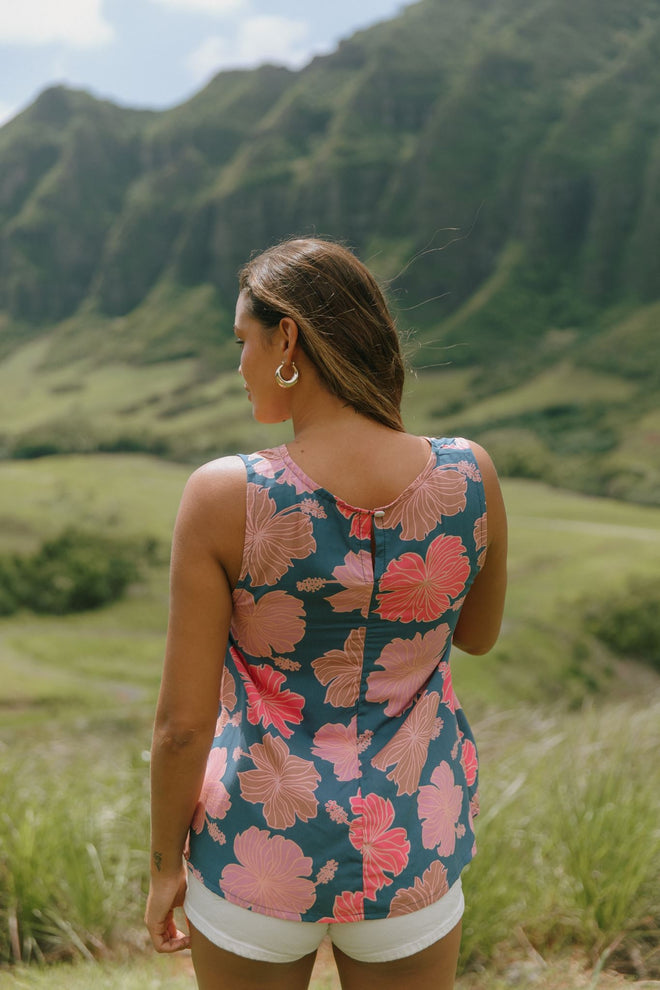 woman with brown hair wearing a navy high neck sleeveless top with bright pink hibiscus print