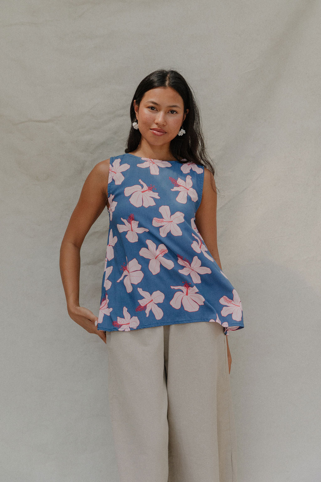 woman with brown hair wearing a navy sleeveless high neck blouse with white hibiscus print