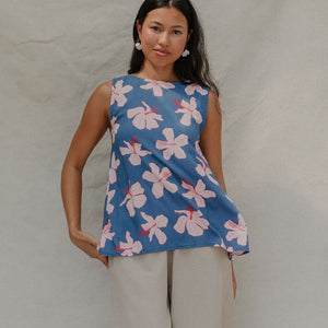 woman with brown hair wearing a navy sleeveless high neck blouse with white hibiscus print