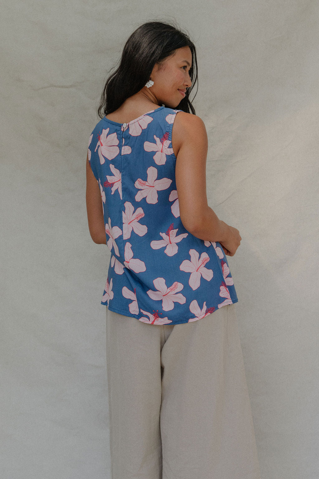 woman with brown hair wearing a navy sleeveless high neck blouse with white hibiscus print