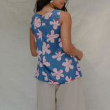 woman with brown hair wearing a navy sleeveless high neck blouse with white hibiscus print