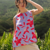 woman with brown hair wearing a sleeveless blouse with periwinkle background and bright red hibiscus print.