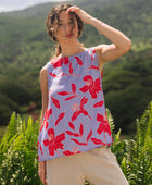 woman with brown hair wearing a sleeveless blouse with periwinkle background and bright red hibiscus print.