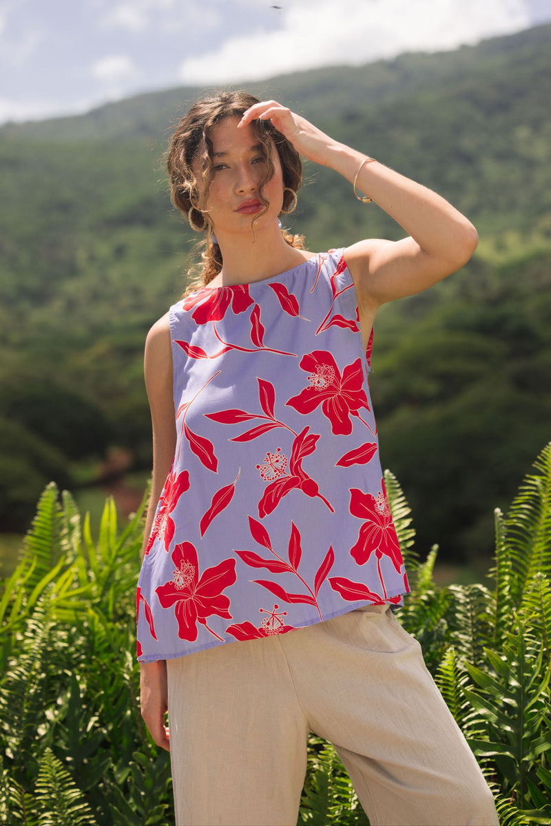 woman with brown hair wearing a sleeveless blouse with periwinkle background and bright red hibiscus print.