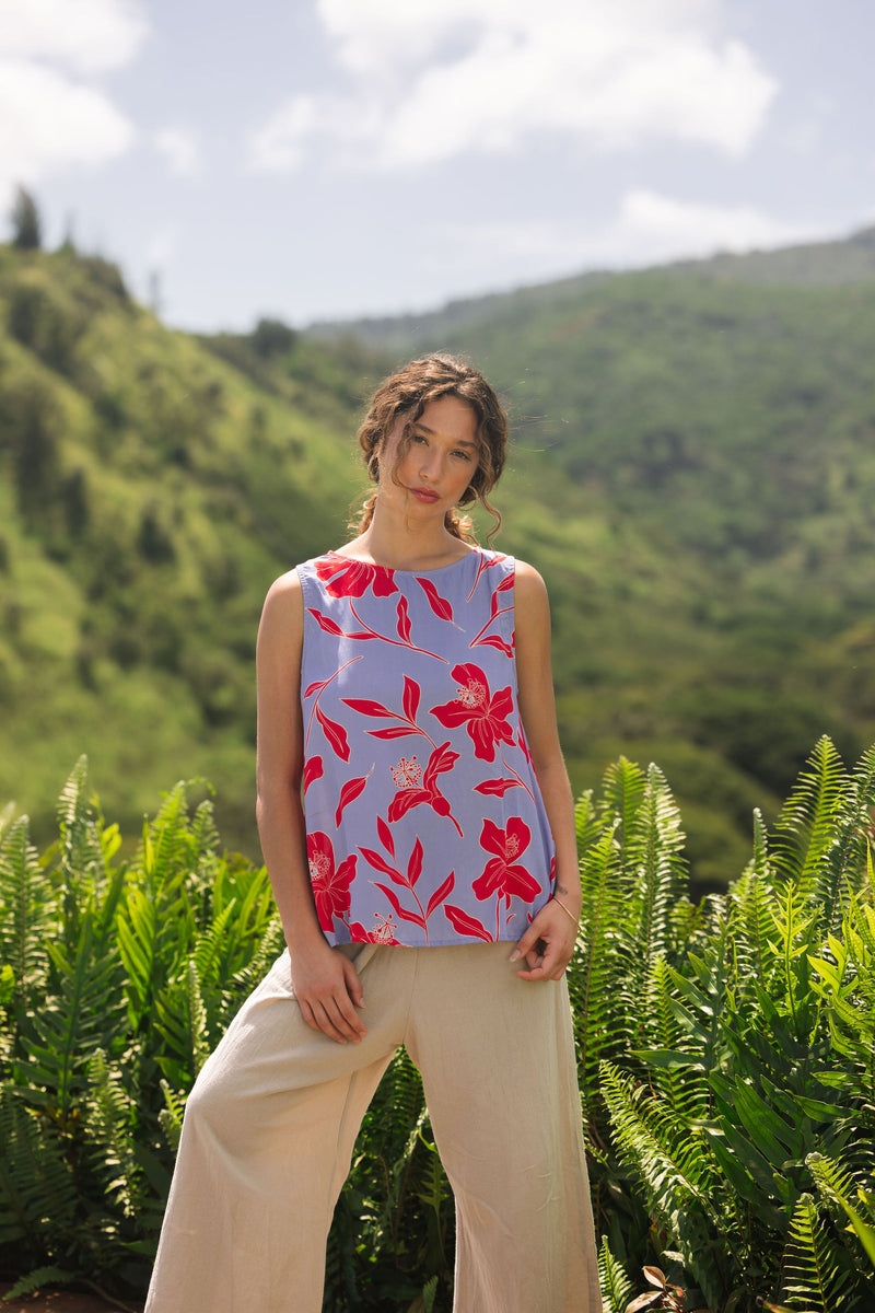 woman with brown hair wearing a sleeveless blouse with periwinkle background and bright red hibiscus print.