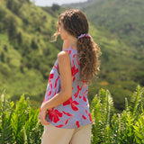 woman with brown hair wearing a sleeveless blouse with periwinkle background and bright red hibiscus print.