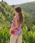 woman with brown hair wearing a sleeveless blouse with periwinkle background and bright red hibiscus print.