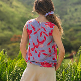 woman with brown hair wearing a sleeveless blouse with periwinkle background and bright red hibiscus print.