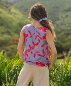woman with brown hair wearing a sleeveless blouse with periwinkle background and bright red hibiscus print.