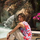 woman with brown hair wearing a sleeveless blouse with periwinkle background and bright red hibiscus print.