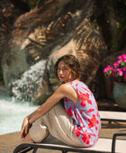 woman with brown hair wearing a sleeveless blouse with periwinkle background and bright red hibiscus print.